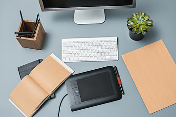 Image showing The gray desk with laptop, notepad with blank sheet, pot of flower, stylus and tablet for retouching