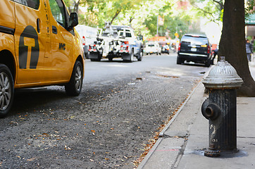 Image showing Black fire hydrant on city sidewalk, traffic passing