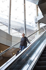 Image showing Businesswoman with large black bag and mobile phone descending on escalator.