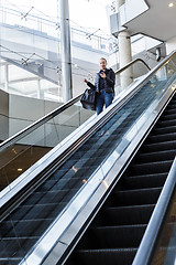 Image showing Businesswoman with large black bag and mobile phone descending on escalator.