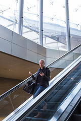 Image showing Businesswoman with large black bag and mobile phone descending on escalator.