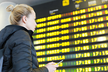 Image showing Woman at airport in front of flight information board checking her phone.