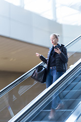 Image showing Businesswoman with large black bag and mobile phone descending on escalator.