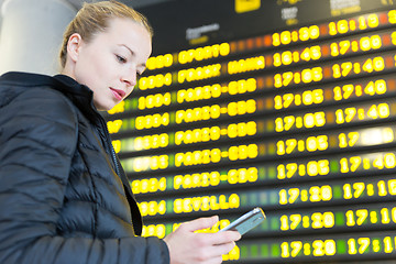 Image showing Woman at airport in front of flight information board checking her phone.