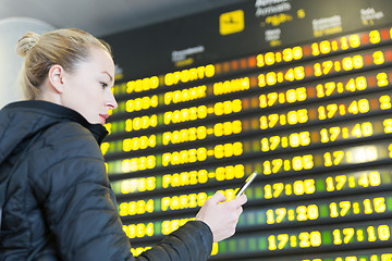 Image showing Woman at airport in front of flight information board checking her phone.