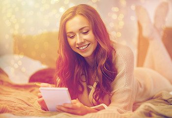 Image showing happy young woman with notebook in bed at home