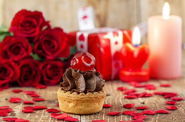 Image showing Cupcake with cherry in front of bouquet of red roses