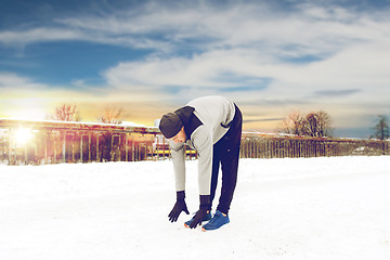 Image showing man exercising and stretching leg on winter bridge