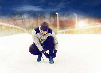 Image showing man with earphones tying sports shoe in winter