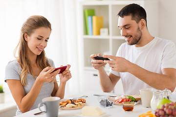 Image showing couple with smartphones having breakfast at home