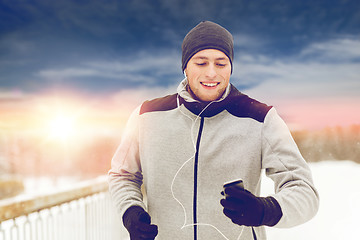 Image showing happy man with earphones and smartphone in winter