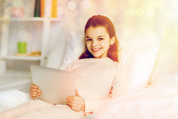 Image showing happy girl lying in bed with tablet pc at home