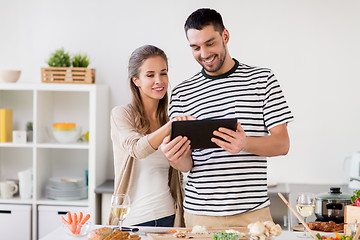 Image showing happy couple with tablet pc cooking food at home