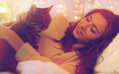 Image showing happy young woman with cat lying in bed at home