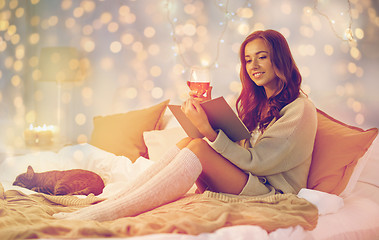 Image showing happy young woman reading book in bed at home