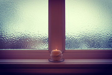 Image showing Burning candle and frosted window in winter twilight