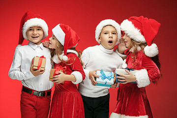 Image showing Two happy girls and boys in santa claus hats with gift boxes