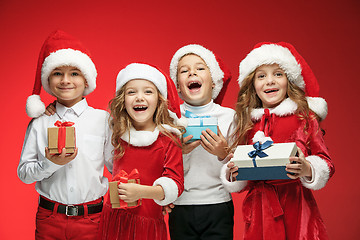 Image showing Two happy girls and boys in santa claus hats with gift boxes