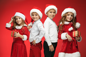 Image showing Two happy girls and boys in santa claus hats with gift boxes