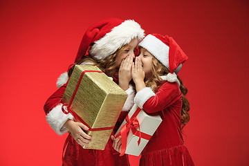 Image showing Two happy girls in santa claus hats with gift boxes at studio