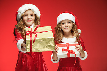 Image showing Two happy girls in santa claus hats with gift boxes at studio