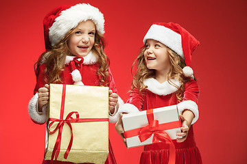 Image showing Two happy girls in santa claus hats with gift boxes at studio