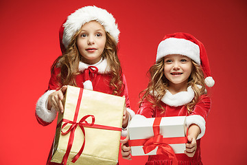 Image showing Two happy girls in santa claus hats with gift boxes at studio