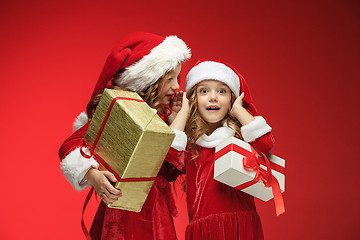 Image showing Two happy girls in santa claus hats with gift boxes at studio