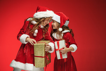 Image showing Two happy girls in santa claus hats with gift boxes at studio