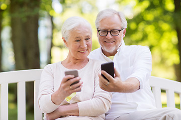 Image showing happy senior couple with smartphones at park