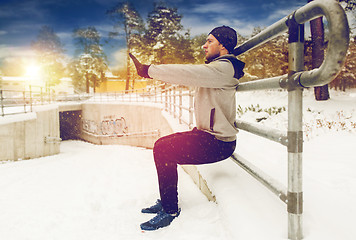 Image showing sports man doing squats at fence in winter