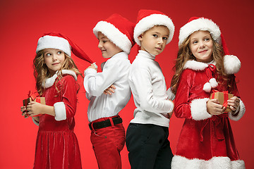 Image showing Two happy girls and boys in santa claus hats with gift boxes at studio