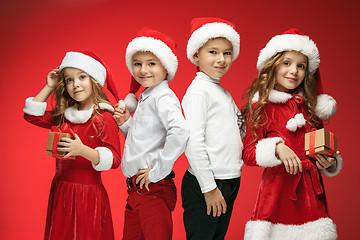 Image showing Two happy girls and boys in santa claus hats with gift boxes at studio