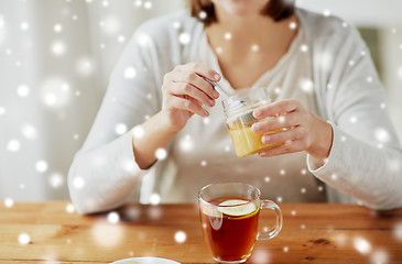 Image showing close up of woman adding honey to tea with lemon