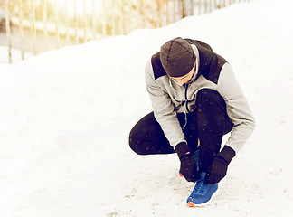 Image showing man with earphones tying sports shoe in winter