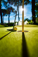 Image showing Mini Golf yellow ball with a bat near the hole at sunset