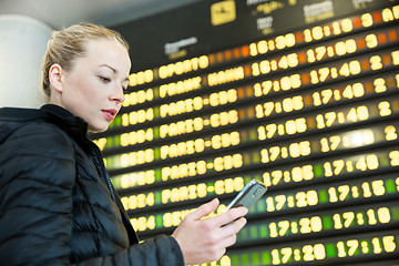 Image showing Woman at airport in front of flight information board checking her phone.
