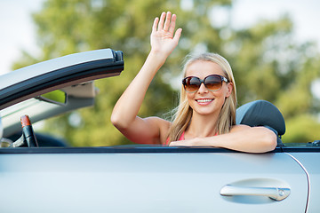 Image showing happy young woman in convertible car waving hand