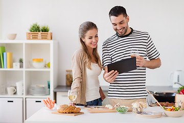 Image showing happy couple with tablet pc cooking food at home