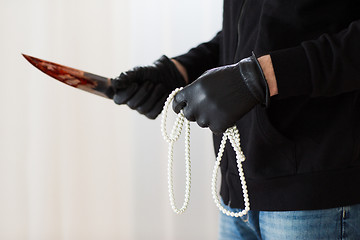 Image showing criminal with knife and jewelry at crime scene