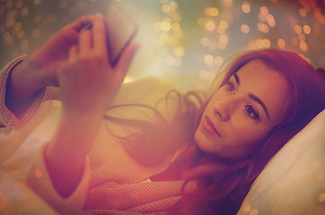 Image showing young woman with smartphone in bed at home bedroom