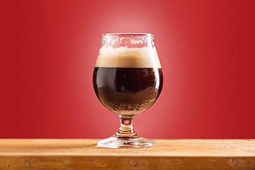 Image showing glass of cold frothy dark beer on an old wooden table