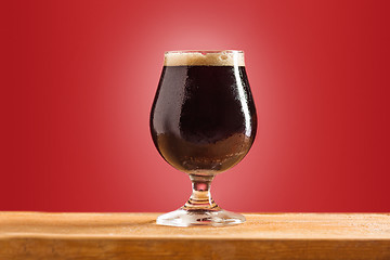 Image showing glass of cold frothy dark beer on an old wooden table