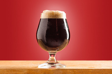 Image showing glass of cold frothy dark beer on an old wooden table