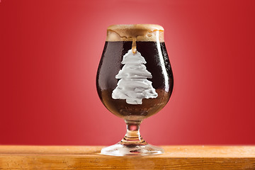 Image showing glass of cold frothy dark beer on an old wooden table