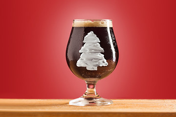 Image showing glass of cold frothy dark beer on an old wooden table