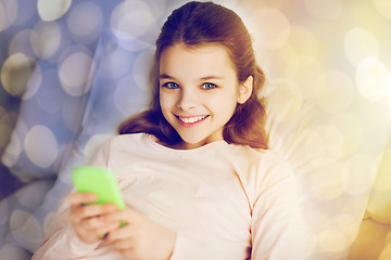 Image showing happy girl in bed with smartphone over lights