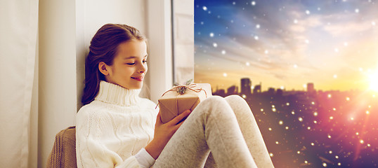 Image showing girl with christmas gift on window sill in winter