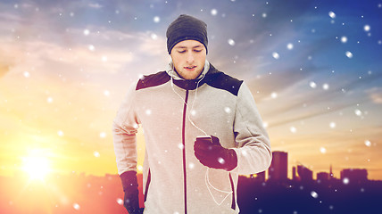 Image showing happy man with earphones and smartphone in winter