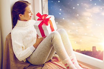 Image showing girl with christmas gift on window sill in winter